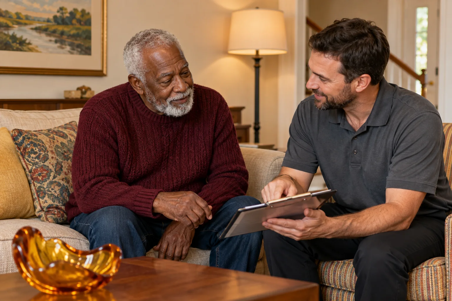 Older adult and home safety representative discussing a tablet on a sofa