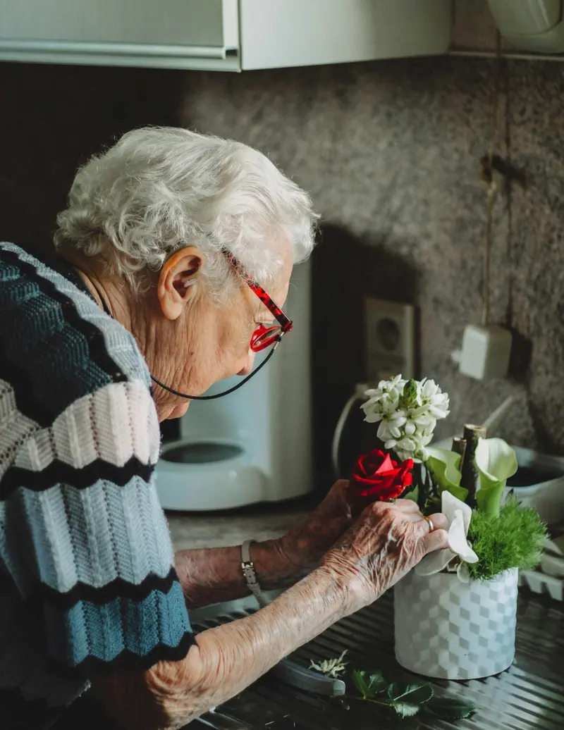 Senior woman arranging flowers by her kitchen window